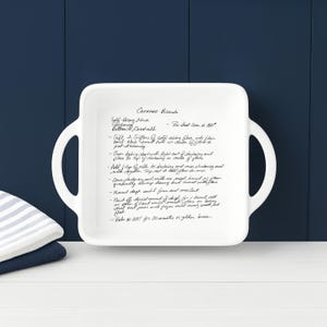 Personalized recipe baking dish, white ceramic casserole dish displayed upright against a navy farmhouse backdrop with folded kitchen towels. Clean, modern presentation of a custom engraved recipe dish ideal for weddings, anniversaries, housewarming gifts, and family recipe keepsakes.
