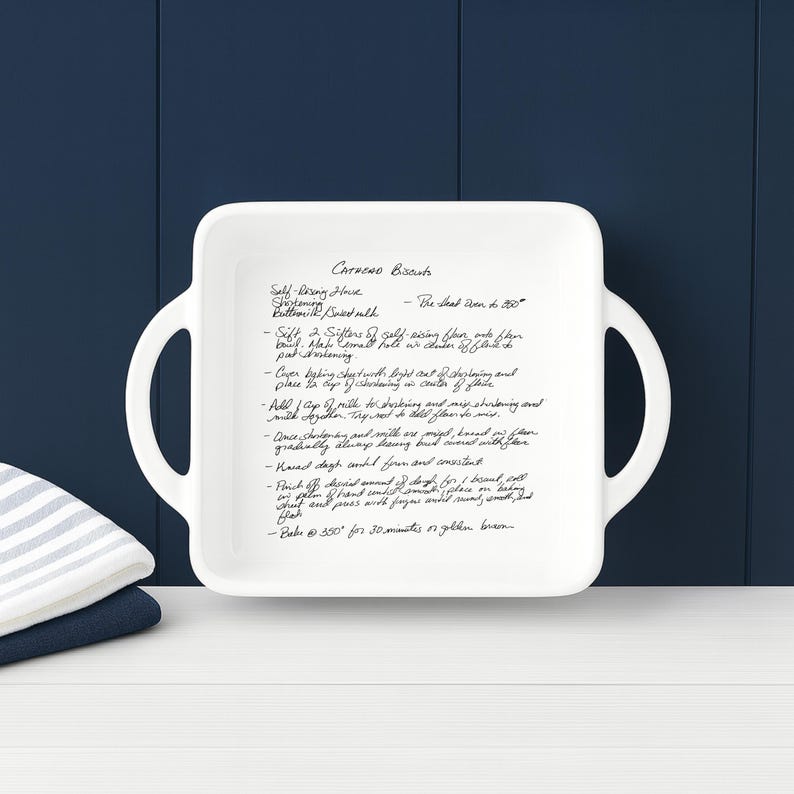 Personalized recipe baking dish, white ceramic casserole dish displayed upright against a navy farmhouse backdrop with folded kitchen towels. Clean, modern presentation of a custom engraved recipe dish ideal for weddings, anniversaries, housewarming gifts, and family recipe keepsakes.