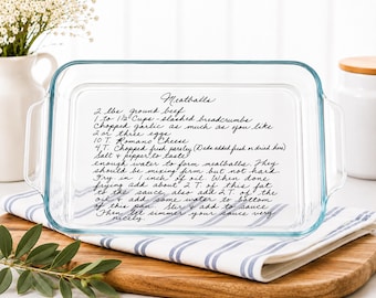 May include: A rectangular clear glass baking dish featuring a black handwritten recipe for meatballs etched onto the bottom surface. The text includes ingredients like ground beef, breadcrumbs, garlic, eggs, Romano cheese, and parsley, along with cooking instructions.