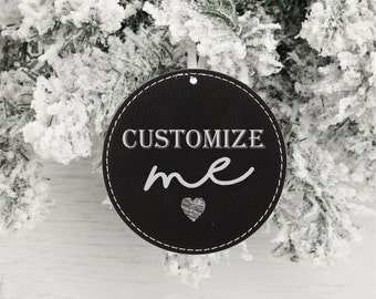 May include: Black round leather ornament with white stitching and the text "CUSTOMIZE me" with a small heart design.