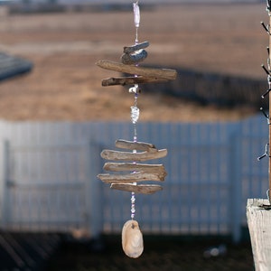 May include: A driftwood and crystal mobile with a seashell hanging at the bottom. The mobile is made of natural materials and has a rustic, bohemian style.