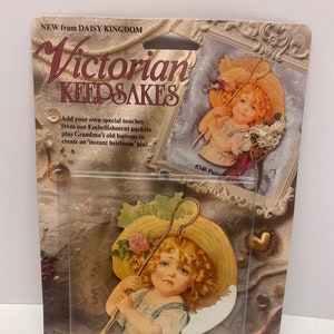 May include: Victorian Keepsakes pin featuring a vintage illustration of a child in a bonnet, holding a walking stick. The pin is packaged on a card with the text "Victorian Keepsakes" and "NEW from DAISY KINGDOM". The pin includes a pin back.