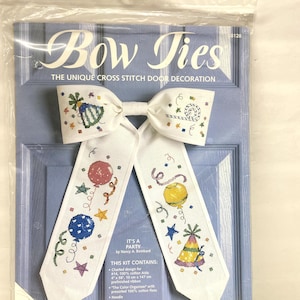 May include: A cross-stitch door decoration kit in a plastic package. The kit features a white bow tie design with colorful party-themed cross-stitch patterns, including balloons, stars, and a party hat. The text "Bow Ties" is at the top.