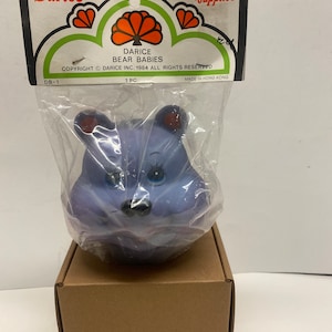 May include: A purple bear head craft supply, packaged in plastic with a Darice label. The label reads "Darice Bear Babies, Copyright Darice Inc. 1984 All Rights Reserved, 1 PC, Made in Hong Kong."