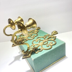 Puede incluir: Dos candelabros de lat&oacute;n dorado adornados con un dise&ntilde;o floral decorativo. Los candelabros son de color dorado y presentan brazos curvos y copas en forma de campana. Los candelabros est&aacute;n sobre una caja de color turquesa.