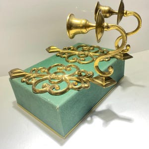 Puede incluir: Un par de candelabros de lat&oacute;n dorado con adornos de volutas y brazos curvos. Montados sobre una caja rectangular de color verde azulado con ribetes dorados. El dise&ntilde;o es cl&aacute;sico y elegante, adecuado para la decoraci&oacute;n del hogar.