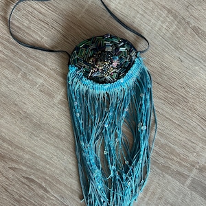 May include: A blue beaded fringe necklace with a black elastic band. The beaded section is round and features a variety of colors and shapes.