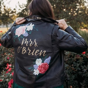 May include: Black leather jacket with a floral design and the text "Mrs. O'Brien" and "Dec. 2, 2020" painted on the back.