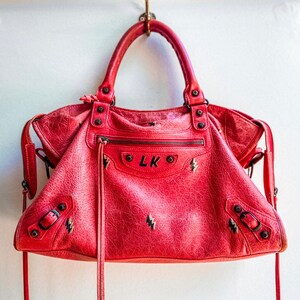 May include: A red leather handbag with black lightning bolt embroidery and the initials "LK" on the front.