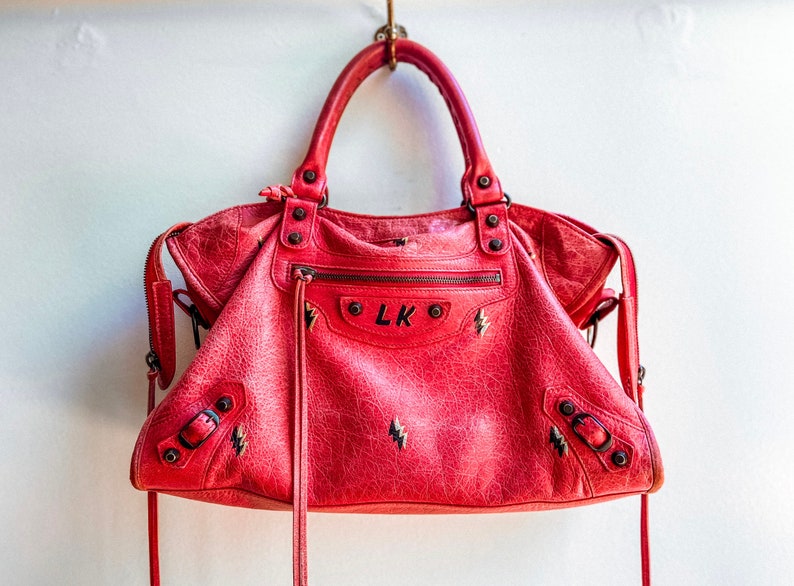 May include: A red leather handbag with black lightning bolt embroidery and the initials "LK" on the front.
