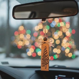 Rustic wood Christmas tree ornament hanging from car mirror with festive bokeh lights.