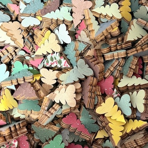 May include: A large collection of small, flat, wooden tree-shaped cutouts in various colors including yellow, sage green, dark green, red, and brown. Some pieces feature a printed pattern of holly leaves and red berries on a white background.