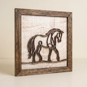 May include: Wooden framed art piece featuring a horse and rider silhouette. The artwork is crafted from layered wood, creating a 3D effect. The frame is a rustic brown, and the background is a distressed white.