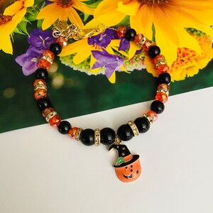 May include: A black and orange Halloween themed bracelet with a pumpkin charm. The bracelet is made of black beads and orange glass beads. The pumpkin charm has a green hat and a smiling face.