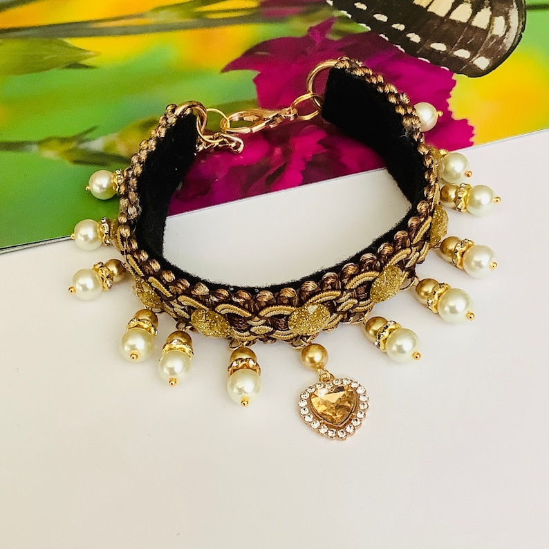 May include: A gold and black bracelet with a heart-shaped pendant and white pearl accents.
