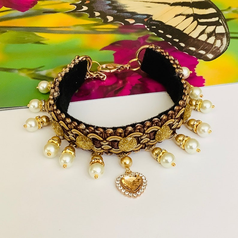 May include: A gold and black choker necklace with a heart-shaped pendant and white pearl accents.