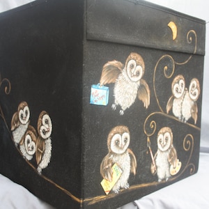 May include: Black storage box with a painted design of owls on a branch. The owls are brown and white with gold accents. The box has a gold crescent moon on the top.