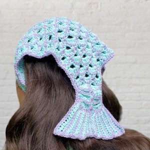 May include: A crocheted mermaid tail headband in shades of light blue and purple. The headband is designed to look like a mermaid's tail with a fin at the bottom.
