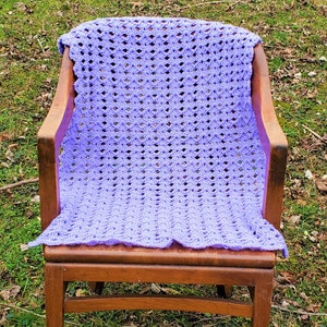 Pu&ograve; includere: Una coperta all'uncinetto color lavanda drappeggiata su una sedia di legno. La coperta ha un motivo a rombi ed &egrave; realizzata con un filato morbido.