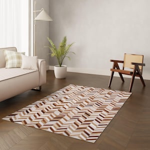 May include: A brown and white cowhide rug with a chevron pattern. The rug is laid out on a hardwood floor in a living room setting.