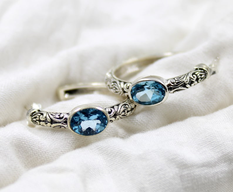 May include: Two silver rings with ornate designs and blue topaz gemstones.