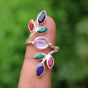 May include: Silver ring with a moonstone and four gemstones set in a leaf design. The gemstones are red, green, and blue.