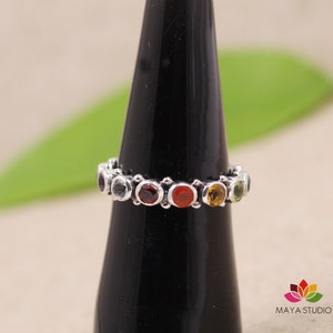 Può includere: Un anello d'argento con una fascia di pietre preziose colorate. Le pietre sono incastonate in un cerchio attorno alla fascia e sono dei colori dell'arcobaleno.