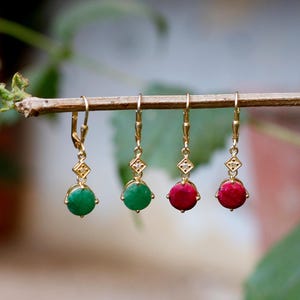 Può includere: Quattro orecchini pendenti color oro con pendenti di pietre preziose. Due orecchini hanno pietre verdi e due hanno pietre rosse. Ogni orecchino presenta un accento a forma di diamante con una piccola gemma.