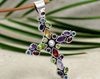 Puede incluir: Un colgante de cruz de plata con una variedad de piedras preciosas, incluyendo amatista, granate, peridoto, piedra lunar y topacio.