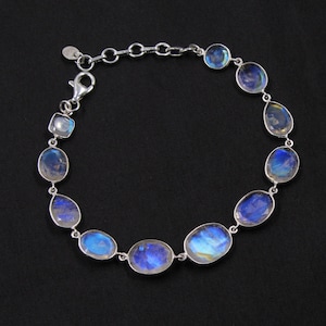 Pode incluir: Uma pulseira de prata com uma série de pedras da lua ovais e iridescentes. As pedras são conectadas por uma delicada corrente de prata, com um fecho de lagosta. As pedras da lua exibem uma cor azul e branca.