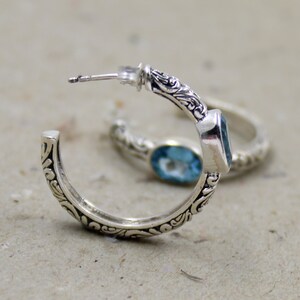 May include: Silver hoop earrings with a blue topaz gemstone set in a floral design.