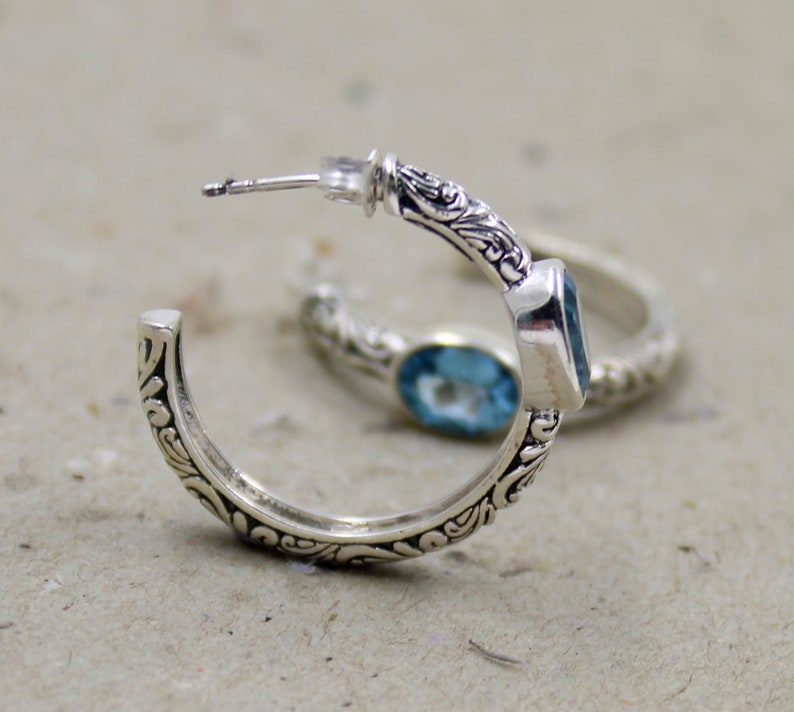 May include: Silver hoop earrings with a blue topaz gemstone set in a floral design.