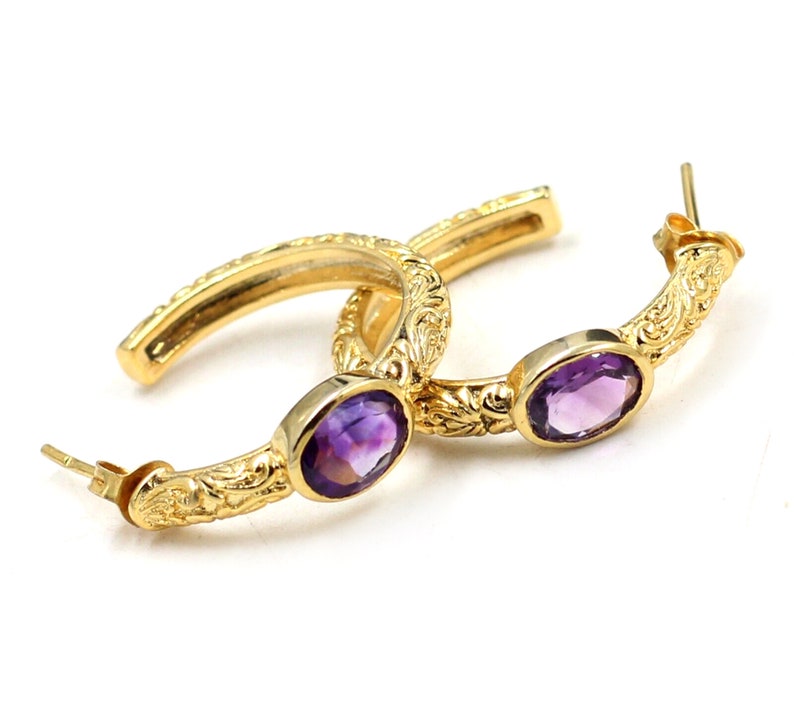 May include: Gold hoop earrings with ornate detailing and purple amethyst gemstones.