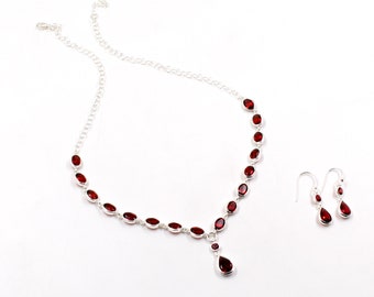 Può includere: Una collana d'argento con un ciondolo a forma di lacrima e orecchini abbinati, entrambi incastonati con pietre preziose rosse. La collana ha una catena delicata ed è adornata con pietre preziose di forma ovale.