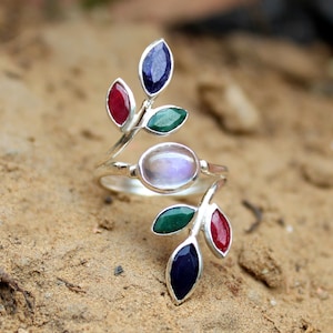 Peut inclure: Une bague en argent avec une pierre de lune centrale et quatre feuilles de pierres précieuses. Les feuilles sont vertes, rouges et bleues.
