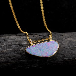 Peut inclure: Un collier délicat en chaîne dorée avec un pendentif orné d'une grande opale irisée sertie dans un cadre en or. L'opale présente une palette de couleurs violette, rose et bleue avec un effet chatoyant. Le pendentif est rehaussé de petits diamants.