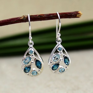 May include: Silver dangle earrings with a teardrop design featuring multiple blue topaz gemstones.