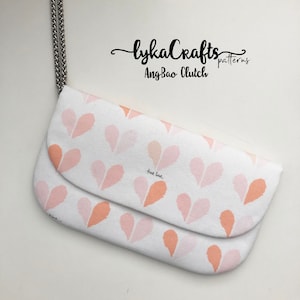 Può includere: Una pochette bianca con un motivo a forma di cuore rosa e arancione. La pochette ha una tracolla a catena argentata e il testo "lykaCrafts patterns AngBao Clutch" è stampato sul davanti. Il testo "true love." è stampato sul lembo interno della pochette.