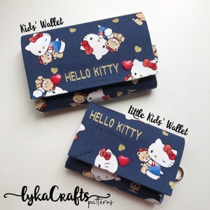 May include: Two navy blue Kids' Wallets with a Hello Kitty pattern. The wallets feature Hello Kitty and teddy bear graphics, red heart accents, and gold lettering that reads "HELLO KITTY". The wallets are a cute accessory for children.