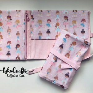Può includere: Un astuccio arrotolato in tessuto rosa con stampa di ballerine e chiusura a zip. L'astuccio ha una tracolla e una fascia in tessuto rosa per fissarlo. Il testo "lykaCrafts patterns rolled up case" è stampato sul tessuto.