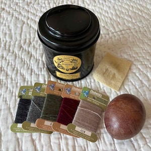 May include: A black tin with a gold label, a small beige square, a wooden egg, and several spools of thread in various colors. The thread spools are labeled "Chadwick's" and are in shades of black, gray, green, and burgundy.