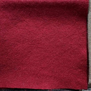 May include: Close-up of three fabric swatches. The primary swatch is a deep red, with a textured surface. Adjacent to it is a gray-green swatch, and a light gray swatch is partially visible on the left. The fabrics appear to be wool or a similar material.