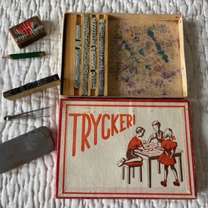 May include: A vintage Tryckeri printing set in a rectangular cardboard box with red text and an illustration of children at a table. The set includes metal type blocks, a wooden storage tray, a small metal tin, tweezers, and a pencil.