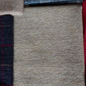 May include: A collection of fabric swatches in various textures and colors. The swatches include a light brown herringbone weave, a dark blue plaid, a solid tan, and a dark blue plaid with red accents. The fabrics appear to be wool or a wool blend.