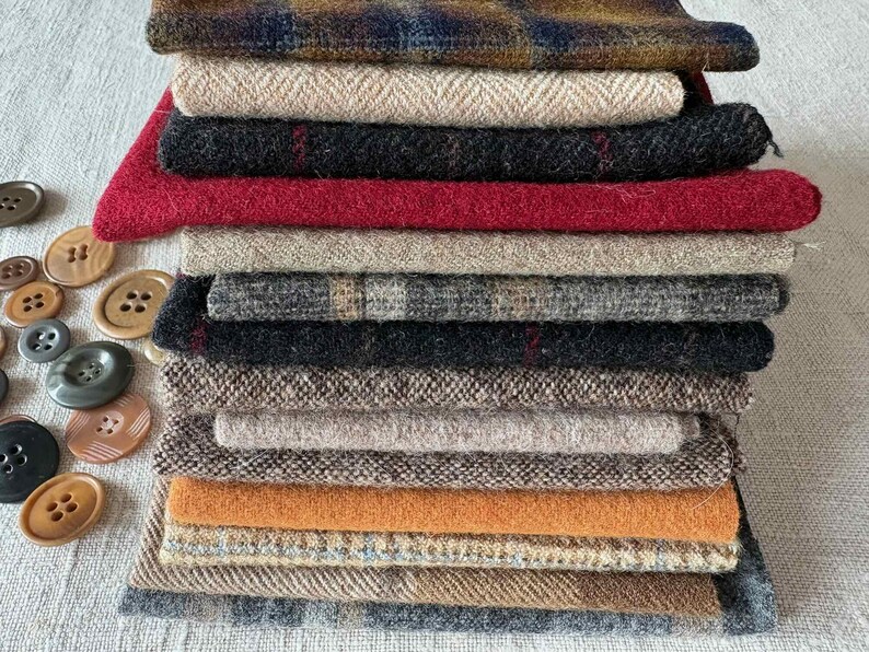 May include: A stack of various fabric swatches in shades of brown, red, black, and beige. The fabrics have different textures and patterns, including herringbone and plaid. Several brown and black buttons are scattered to the left of the fabric stack.