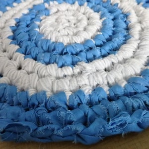 May include: A round, crocheted rug with a blue and white pattern. The rug is made of fabric strips and has a fringed edge.