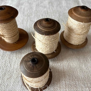 May include: Four wooden spools of varying sizes, each featuring a dark brown finish with concentric circular detailing on the top and bottom discs. Each spool is wrapped with a thick, natural-coloured, fibrous twine or cord material.