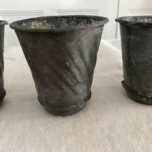 May include: Three grey metal planters with a textured, swirl design. The planters are empty and sitting on a white surface.