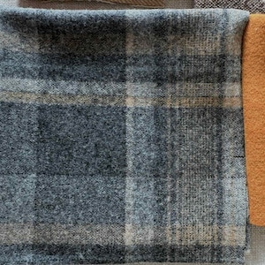 May include: Close-up of fabric swatches. The main swatch is a blue and gray plaid pattern. Adjacent is a solid orange swatch. The fabrics appear to be wool or a similar textured material, suitable for apparel or home decor.