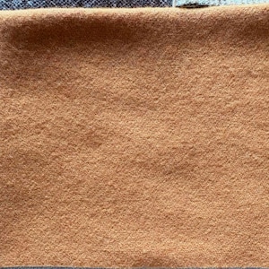 May include: A square of tan fabric with a textured surface. The fabric is surrounded by other fabrics in shades of blue and brown.